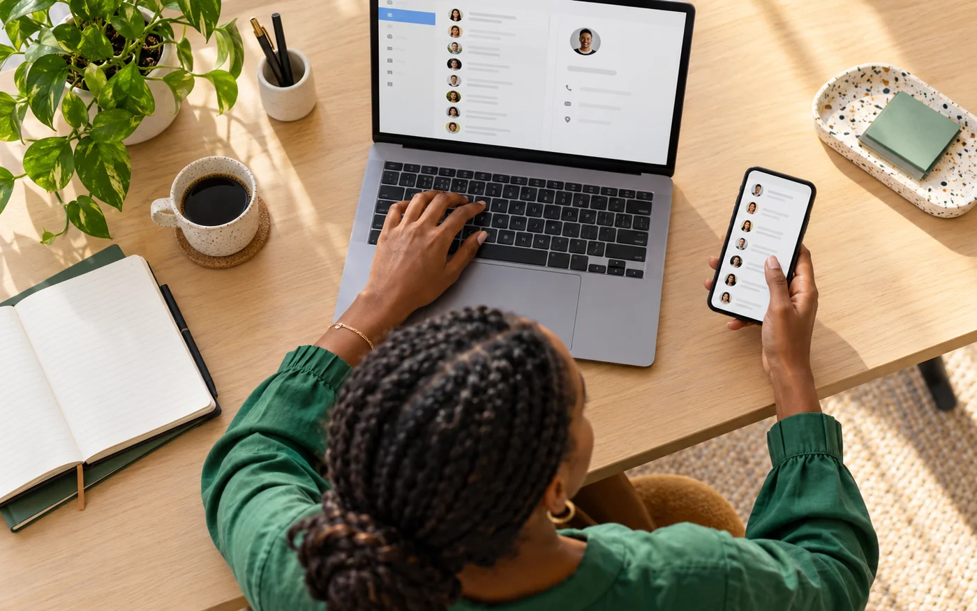 Business owner organizing contacts on a laptop and phone in a bright workspace